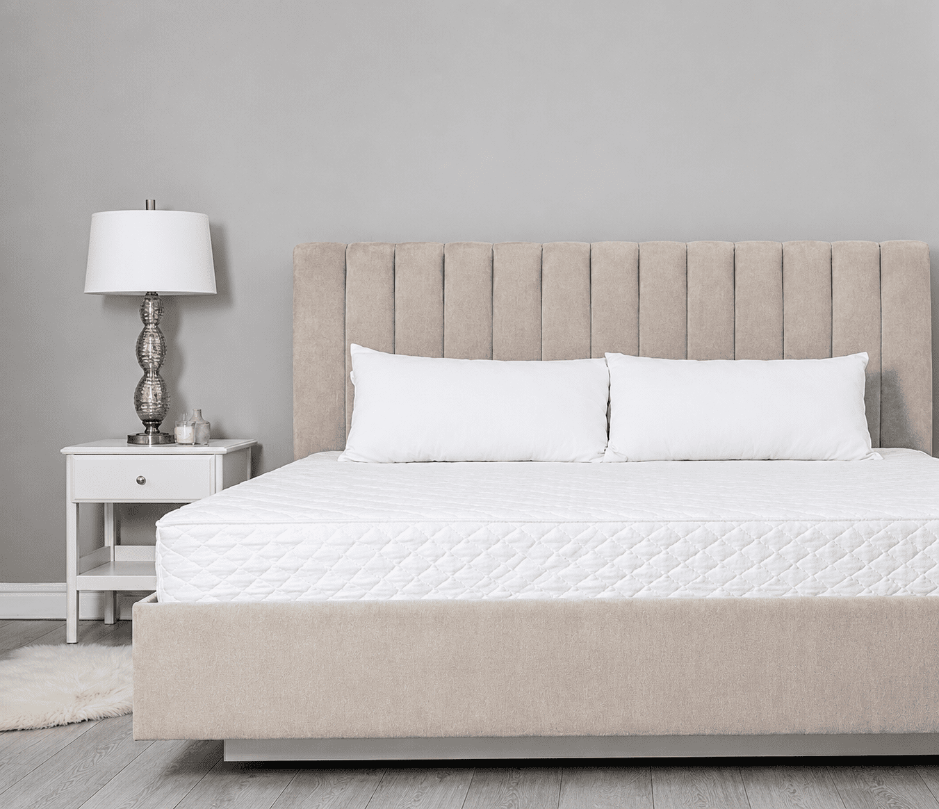 Beige bed with white pillows and lamp.