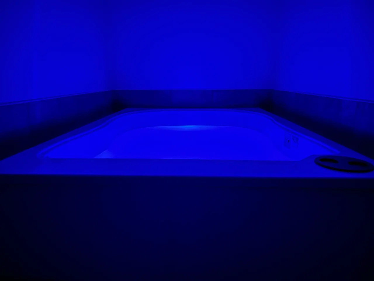 Blue-lit hot tub in dark minimalist room
