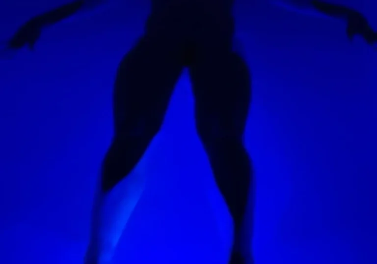 Silhouetted person floating in blue-lit water