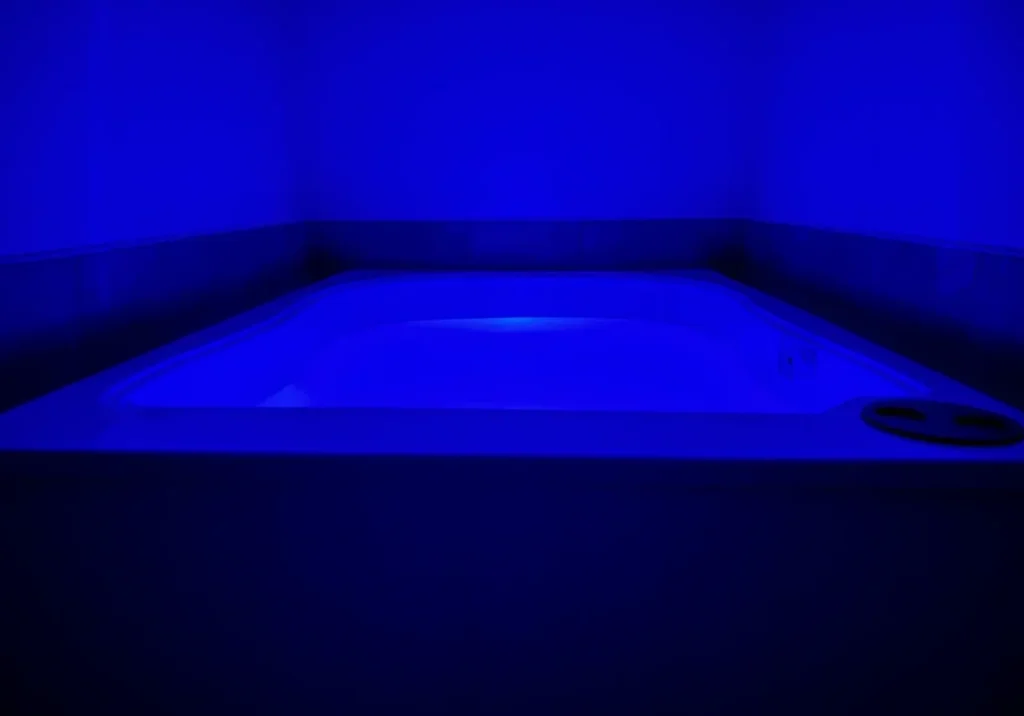 Blue-lit hot tub in dark minimalist room